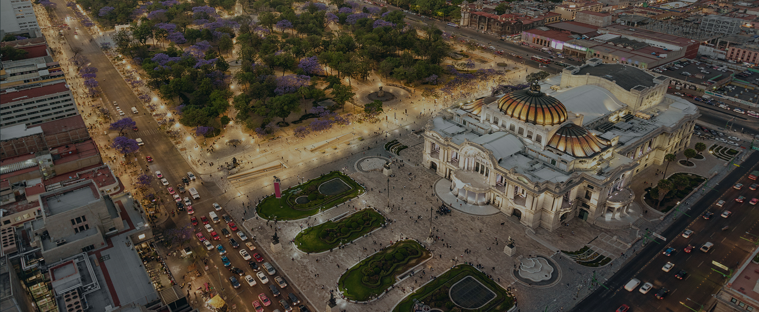 Vista aérea nocturna del Palacio de Bellas Artes y la Alameda Central en Ciudad de México, rodeados por avenidas iluminadas y tráfico urbano.