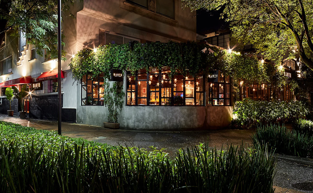 Restaurante elegante junto al Parque Lincoln en Polanco, Ciudad de México, iluminado de noche y rodeado de árboles y áreas verdes en una calle exclusiva y tranquila.