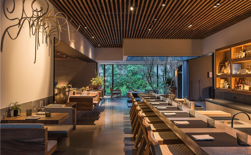 Interior elegante de un restaurante dentro de un hotel boutique en Polanco, Ciudad de México, con diseño contemporáneo, iluminación cálida, mobiliario de madera y vista a un jardín interior.