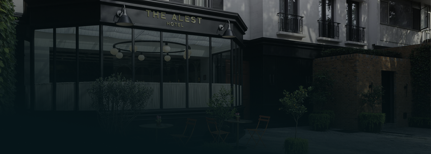 Entrada de hotel boutique con letrero “The Alest Hotel”, ventanales amplios, terraza con mesas y sillas, y vegetación en la acera en Polanco.